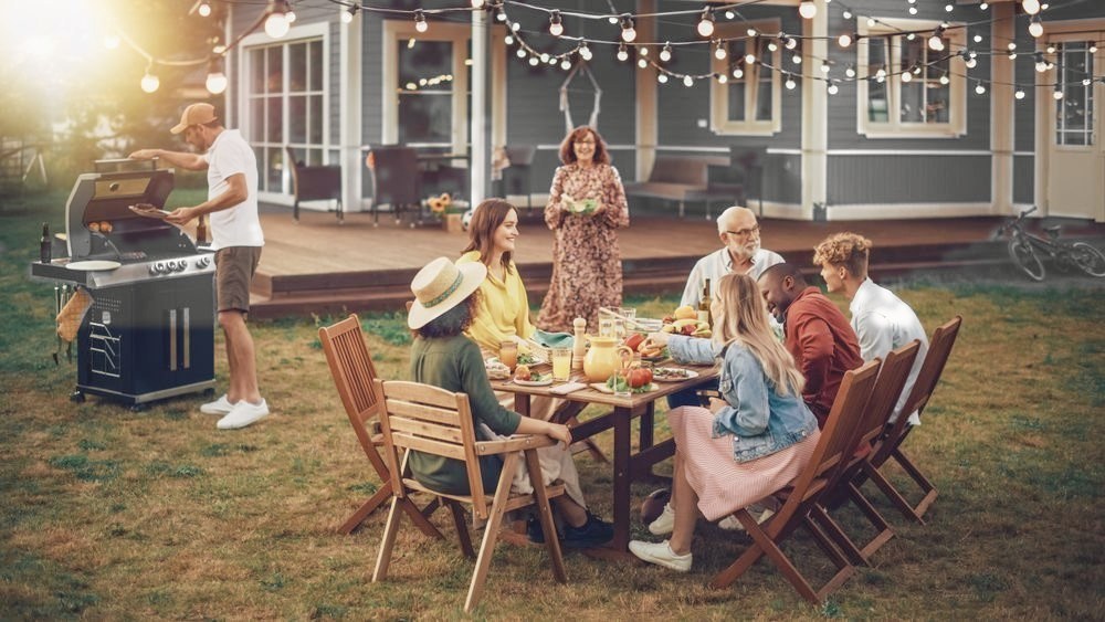Family and friends of several generations gathered around an outdoor table at a home.
